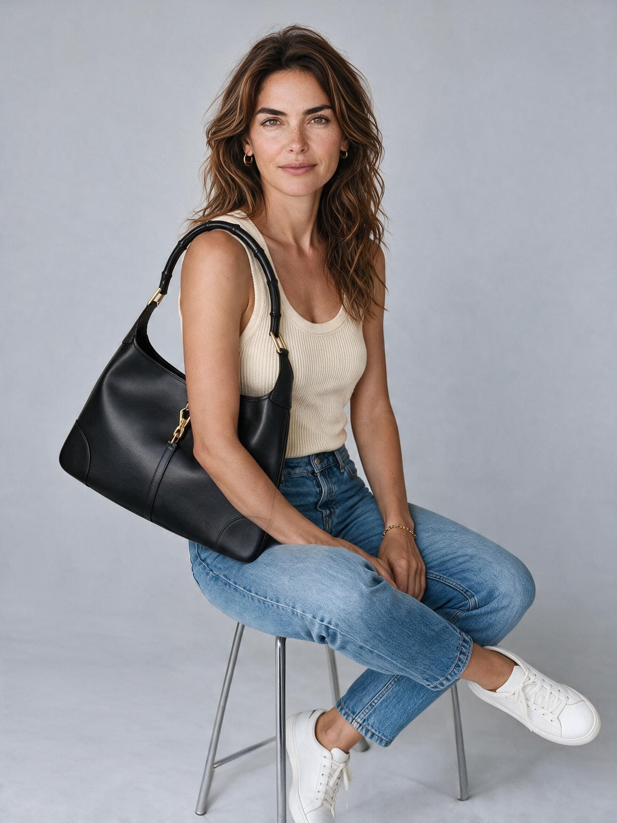 Modella indossa borsa a spalla Borse Vintage in pelle nera con manico effetto bambù e chiusura dorata su sfondo grigio