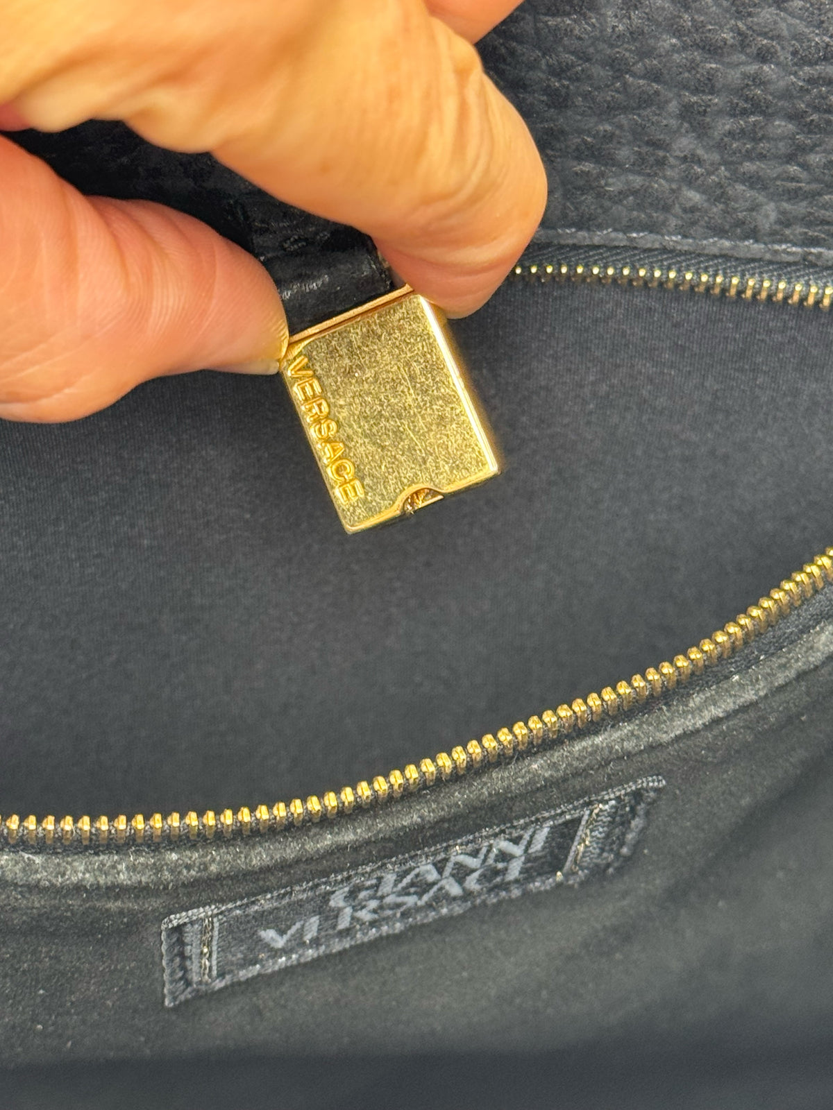 Dettaglio interno della borsa Borse Vintage Gianni Versace con cerniera dorata e logo inciso su tiralampo