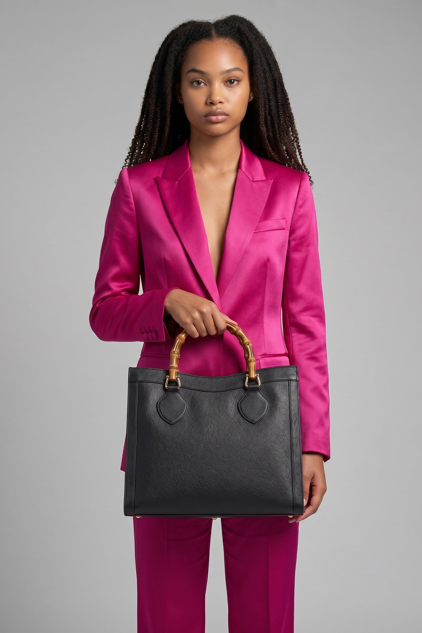 Modella indossa un tailleur fucsia mentre tiene una borsa tote Borse Vintage Gucci nera in pelle con manico in bambù