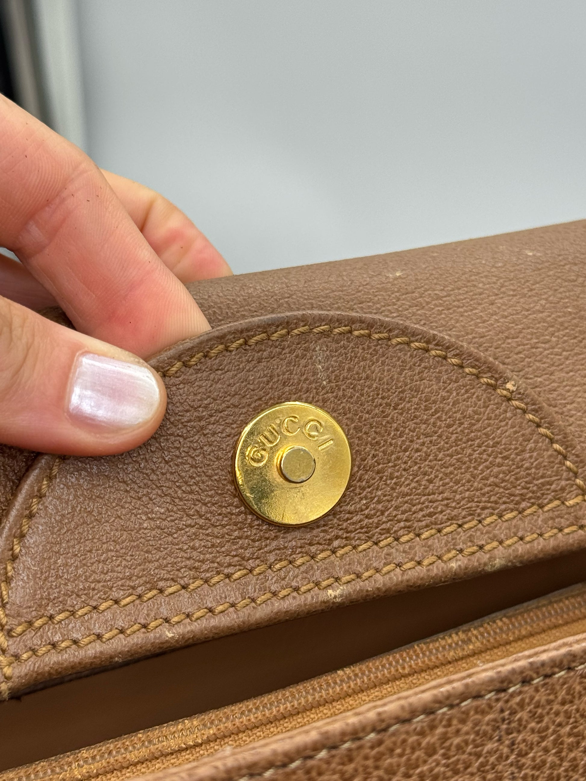 Dettaglio della chiusura magnetica dorata con logo Gucci su borsa Borse Vintage in pelle martellata marrone