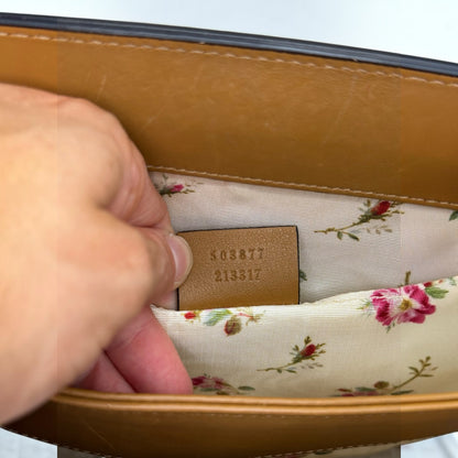 Dettaglio interno borsa Borse Vintage Gucci con etichetta in pelle, codice seriale e fodera in tessuto floreale.