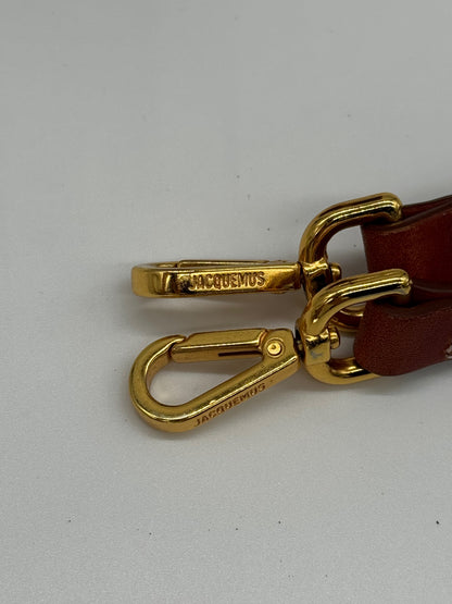 Dettaglio dei moschettoni dorati con logo Borse Vintage Jacquemus su tracolla in pelle color cuoio