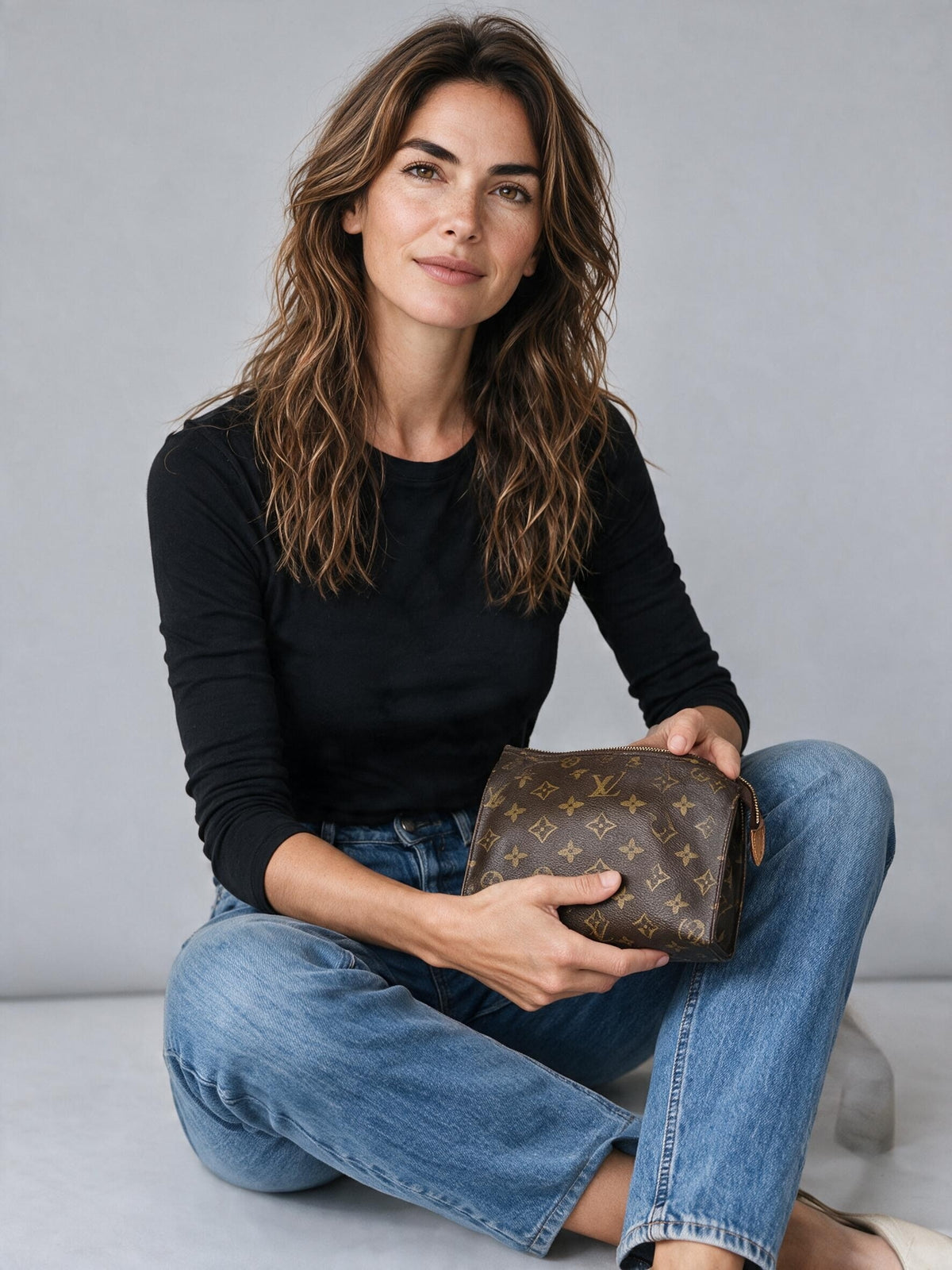 Modella che tiene una pochette Louis Vuitton in tela Monogram marrone, proposta da Borse Vintage su sfondo neutro.