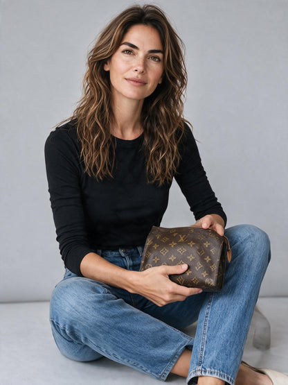 Modella che tiene una pochette Louis Vuitton in tela Monogram marrone, proposta da Borse Vintage su sfondo neutro.