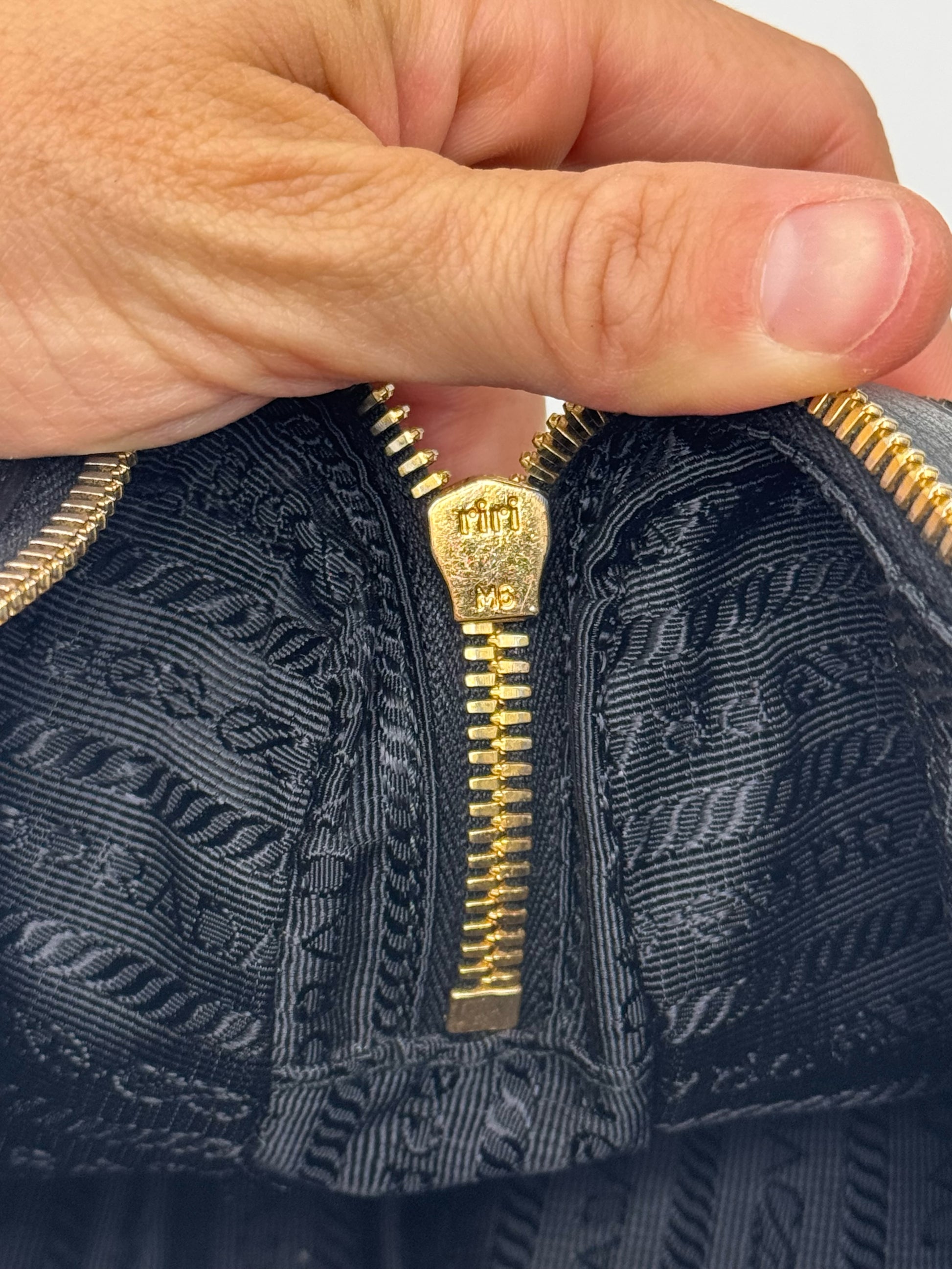 Dettaglio della chiusura zip dorata con logo Borse Vintage su borsa Prada in pelle nera con interno logato