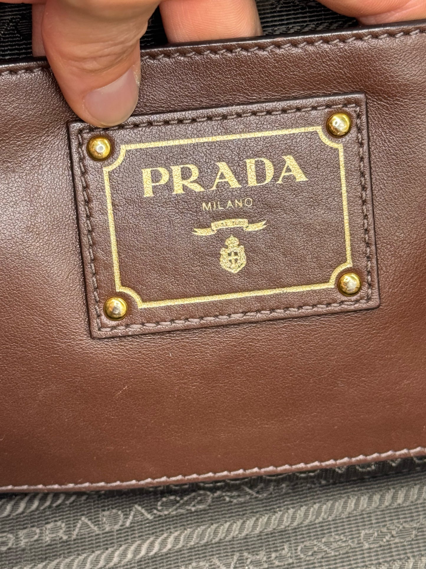 Dettaglio del logo Prada su placca in pelle marrone con borchie dorate, offerto da Borse Vintage